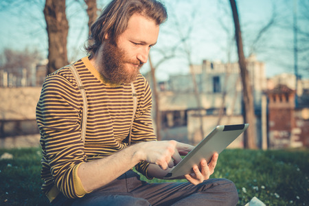young bearded stylish handsome hipster man using tablet outdoorsの写真素材