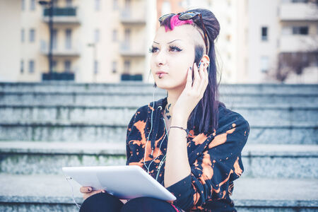 young beautiful punk dark girl listening music in urban landscapeの写真素材