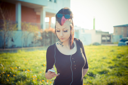 young beautiful punk dark girl listening music  in urban landscapeの写真素材