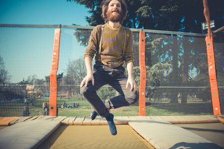 young bearded stylish handsome hipster man jumping on trampoline at playground の写真素材