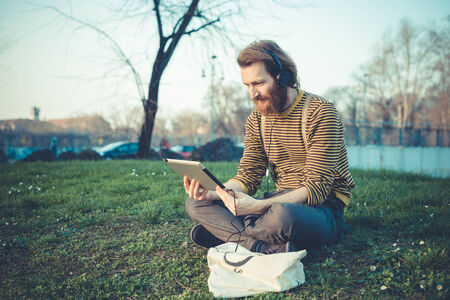 young bearded stylish handsome hipster man using tablet outdoors