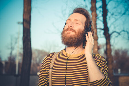 young bearded stylish handsome hipster man listening music with headphones outdoorsの写真素材