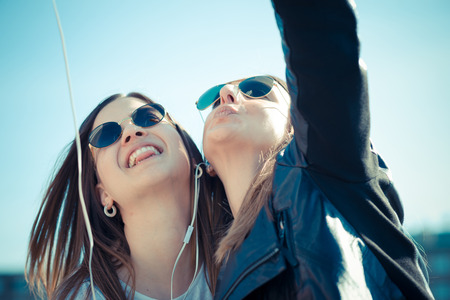 two beautiful young women using smart phone for selfie in the cityの写真素材