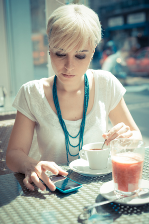 beautiful young blonde short hair hipster woman using smart phone at the cafeの写真素材
