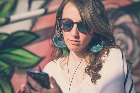 young beautiful brunette woman with smart phone listening music in the cityの写真素材