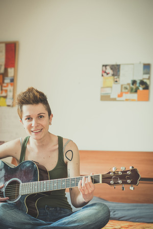 young lesbian stylish hair style woman playing guitar at home の写真素材