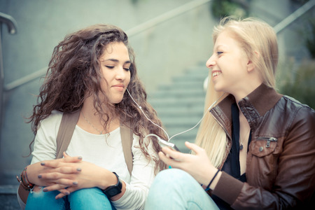 blonde and brunette beautiful stylish young women using smart phone in the cityの写真素材