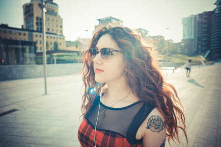 young beautiful hipster woman with red curly hair listening music in the cityの写真素材