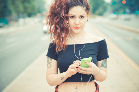 young beautiful hipster woman with red curly hair listening music in the cityの写真素材