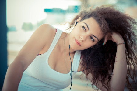 young beautiful long curly hair hipster woman listening to music with tablet in the city