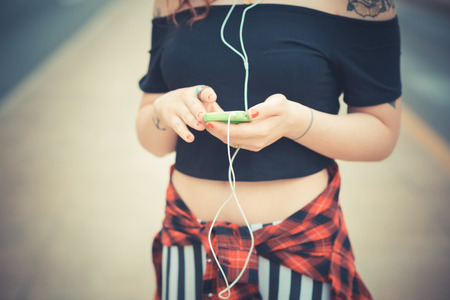 young beautiful hipster woman with red curly hair listening music in the cityの写真素材