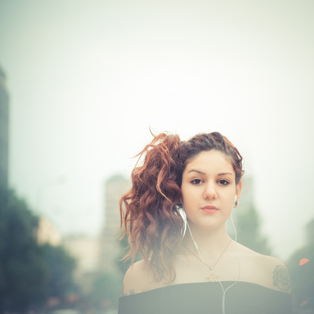 young beautiful hipster woman with red curly hair listening music in the cityの写真素材