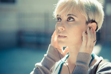 beautiful young blonde short hair hipster woman listening music earphones in the cityの写真素材