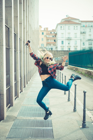 beautiful young blonde hair woman hipster jumping and dancing listening music in the cityの写真素材