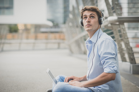 young model hansome blonde man with notebook and headphones in the city