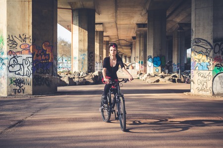 young beautiful punk dark girl riding bike in urban landscapeのeditorial素材