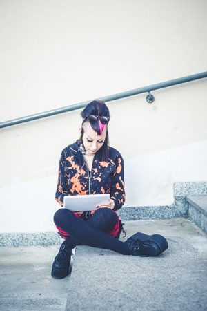 young beautiful punk dark girl using tablet in urban landscapeの写真素材