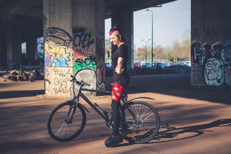 young beautiful punk dark girl riding bike in urban landscapeのeditorial素材
