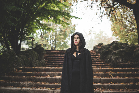 beautiful dark vampire woman with black mantle and hood halloweenの写真素材