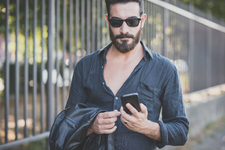 young handsome attractive bearded model man using smartphone in urban contextの写真素材