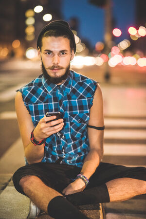 young handsome bearded hipster man using smartphone and listening music with earphones in the cityの写真素材