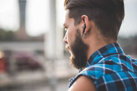 young handsome bearded hipster man using smartphone and listening music with earphones in the cityの写真素材