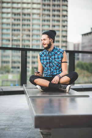 young handsome bearded hipster man using smartphone and listening music with earphones in the cityの写真素材