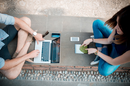 young couple using technology multitasking smarpthone tablet and notebook in the streetの写真素材
