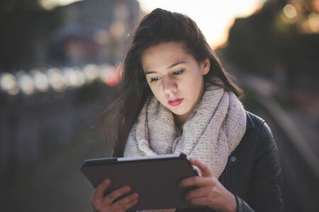 young beautiful long hair woman in town during sunset backlight using tabletの写真素材