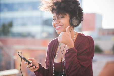 beautiful black curly hair african woman listening music with headphones in townの写真素材
