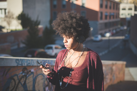 beautiful black curly hair african woman listening music with headphones in townの写真素材