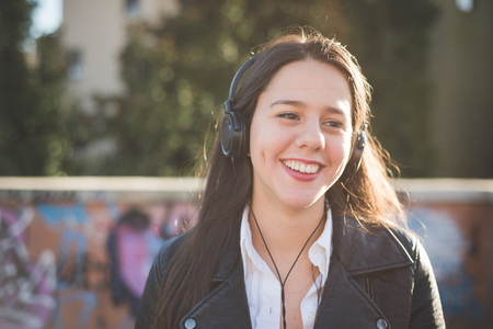 young beautiful long hair woman in town during sunset backlight listening music with headphonesの写真素材