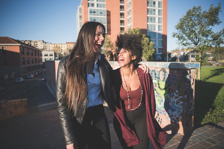 two multiethnic beautiful young woman black and caucasian having fun in townの写真素材