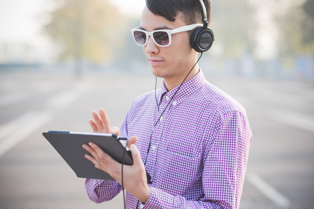 young crazy funny asian man in town outdoor lifestyle listening music with headphones and tablet
