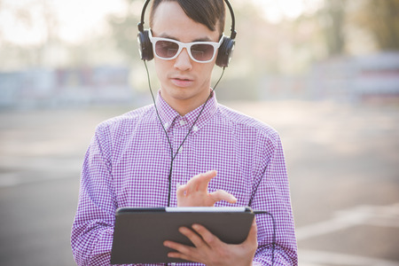 young crazy funny asian man in town outdoor lifestyle listening music with headphones and tabletの写真素材