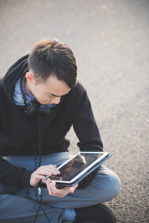 young crazy funny asian man in town outdoor lifestyle listening music with headphones and tabletの写真素材