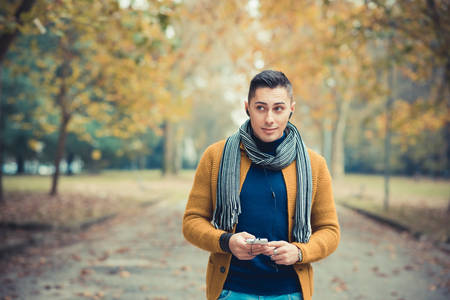 young handsome caucasian man in autumn park outdoor - using smartphone with earphonesの写真素材