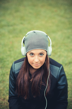 young beautiful brunette straight hair woman in the park during autumn season - listening music with headphonesの写真素材