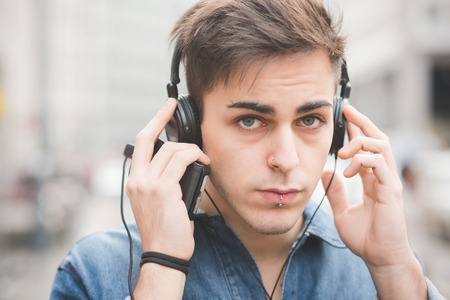 young handsome alternative dark model man in town listening to music with headphones and smartphone...
