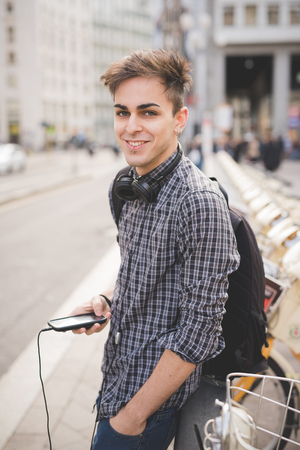 young handsome alternative dark model man in town listening to music with headphones and smartphone connected wirelessの写真素材