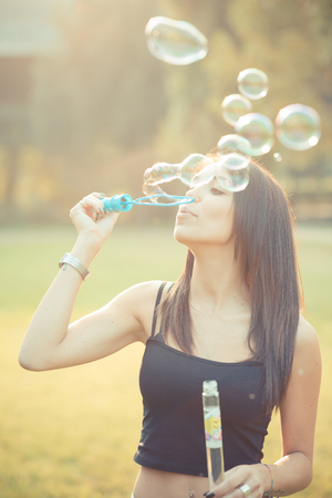 young beautiful brunette straight hair woman blowing soap bubbles outdoorの写真素材