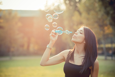 young beautiful brunette straight hair woman blowing soap bubbles outdoorの写真素材