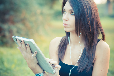 young beautiful brunette straight hair woman using tablet and smartphone sitting on grass outdoorの写真素材