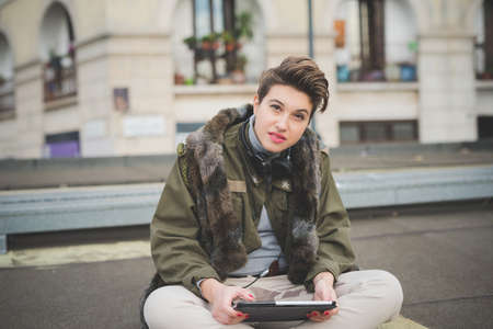 young beautiful short hair hipster woman in town using tablet technological device connected...