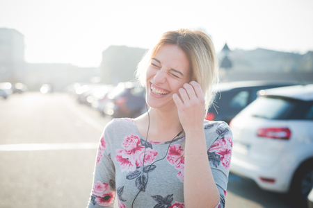 young beautiful blonde woman outdoor in the street of the city listening music and using smartphone with earphonesの写真素材