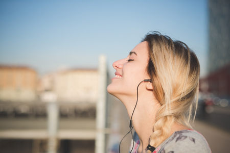 young beautiful blonde woman outdoor in the street of the city listening music and using smartphone with earphonesの写真素材