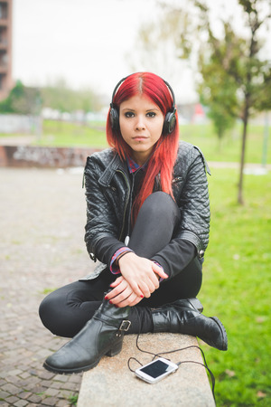 young beautiful red hair venezuelan woman lifestyle in the city of milan outdoor street listening music with headphonesの写真素材