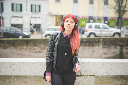 young beautiful red hair venezuelan woman lifestyle in the city of milan outdoor street listening music with headphonesの写真素材