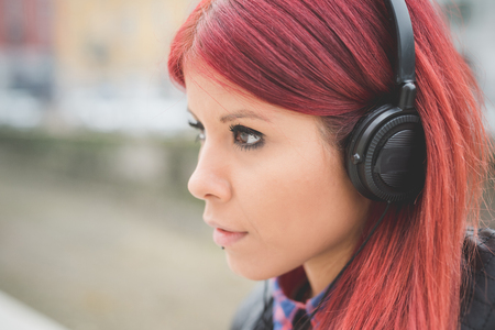 young beautiful red hair venezuelan woman lifestyle in the city of milan outdoor street listening music with headphonesの写真素材