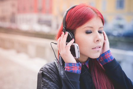 young beautiful red hair venezuelan woman lifestyle in the city of milan outdoor street listening music with headphonesの写真素材